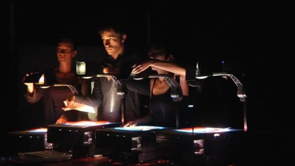 Three people work with projectors in a dark room
