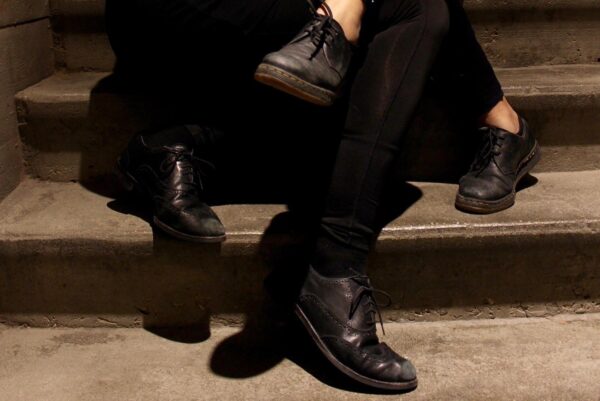 Close up of two sets of legs wearing black pants and black loafers entangled on a set of stairs