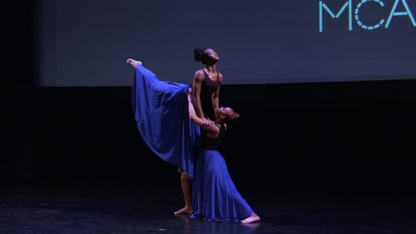 Two dancers on stage in flowy blue dresses, one lifts the other in the air
