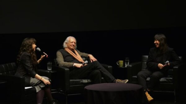 Three people sit in black chairs on a black stage