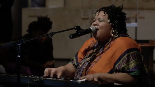 A person sits at a piano while singing into a microphone