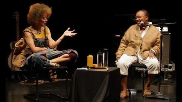 Two people sitting on a black stage with a table between them