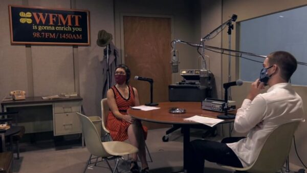 Two people talk in a radio station recording booth