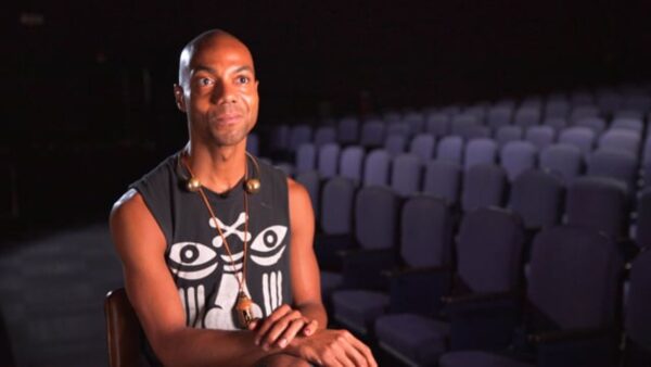 A person sits in front of rows of blue theater seats, lit only by a light coming from their left