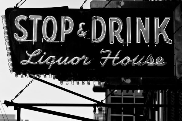 Black and white photo of an old neon business sign that reads Stop and Drink in large straight text and Liquor House in smaller cursive font