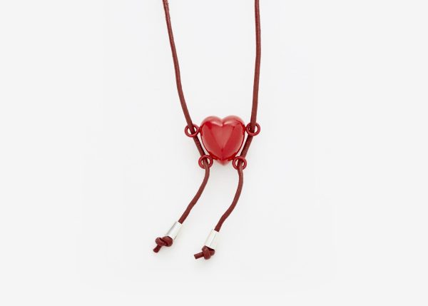 A red cord with a red heart pendant has four clasps, two on each side that make it look like a heart holding onto a swing with legs swinging to left.