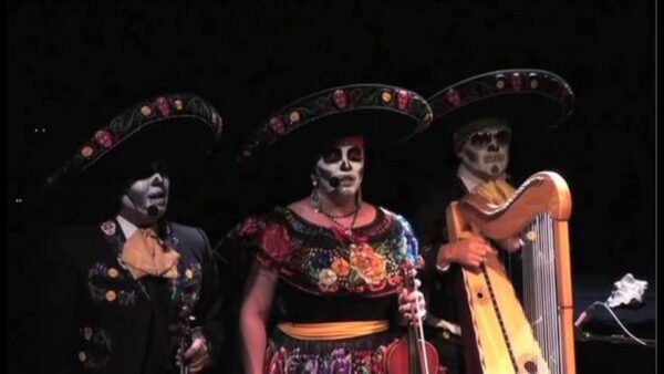 Three mariachi performers in day-of-the-dead paint on a dark stage
