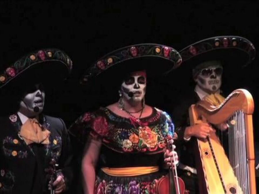 Three mariachi performers in day-of-the-dead paint on a dark stage