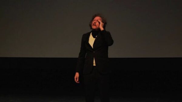 A man rubs his head on a dark stage