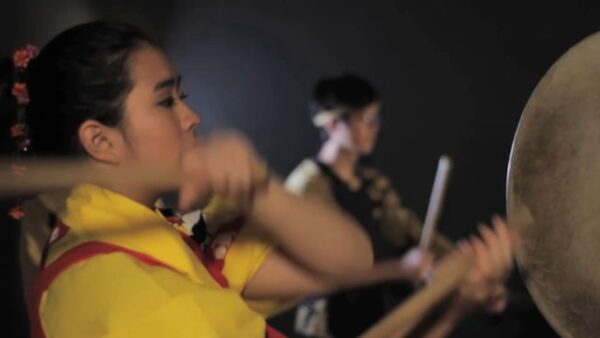 Close up of a person beating on a drum on a stage with another drummer