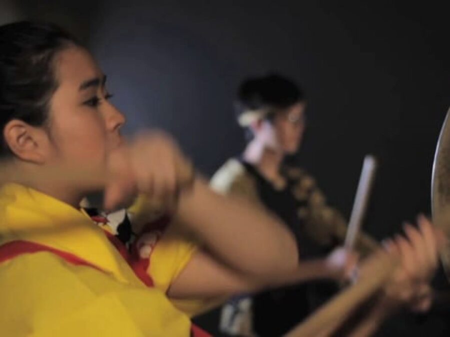 Close up of a person beating on a drum on a stage with another drummer