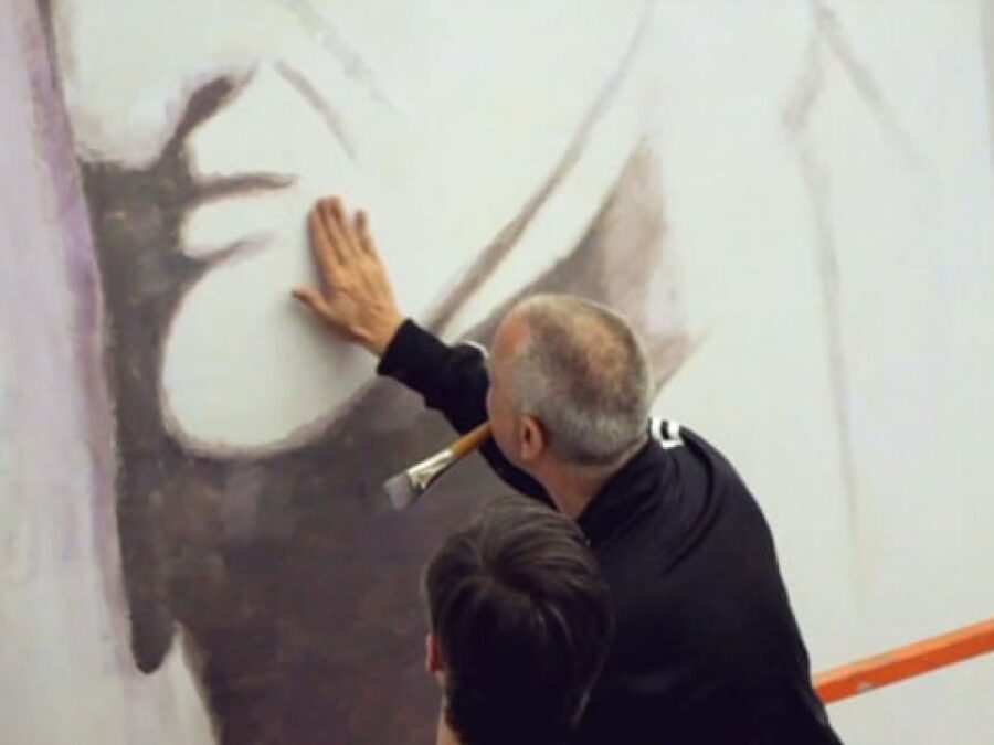 Two people face a wall with black paint on it