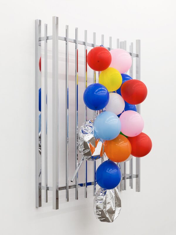 Colorful balloons tied to a window cage hanging against a solid white wall
