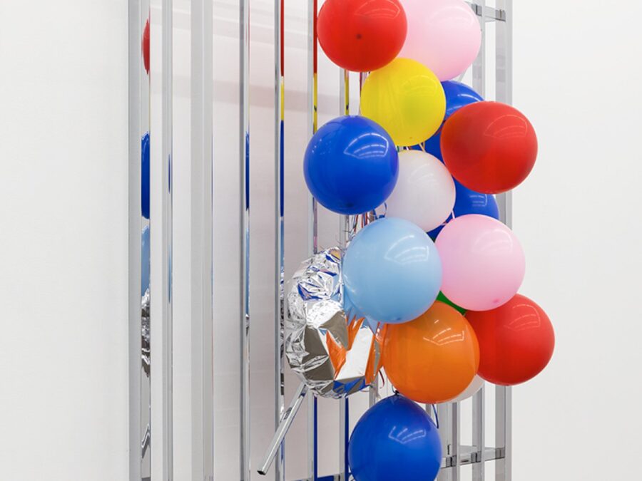 Colorful balloons tied to a window cage hanging against a solid white wall