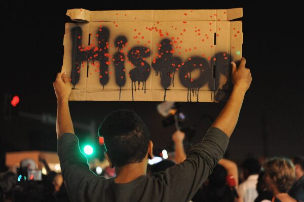 A person holds up a handmade cardboard sign reading History in a crowd at night