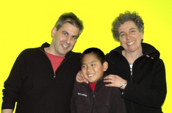 Two adults and a child pose in front of a bright yellow backdrop