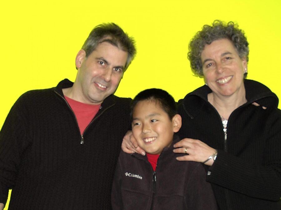 Two adults and a child pose in front of a bright yellow backdrop