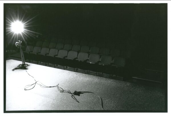 A cord leads to a stand with a bright light on it on a stage in front of an empty theater