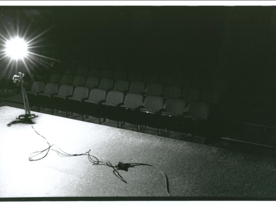 A cord leads to a stand with a bright light on it on a stage in front of an empty theater