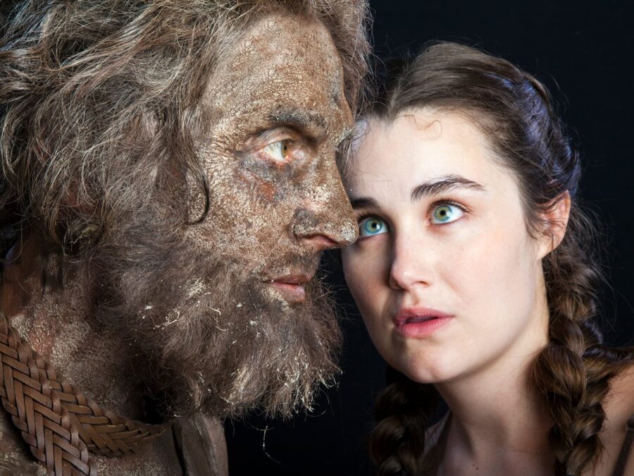 Closeup image of a person dressed as a wolfman posed in profile next to a female looking directly up at him with bright blue eyes