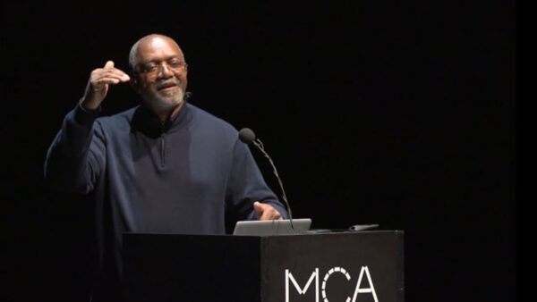 A man speaking from behind a podium marked MCA on a black stage