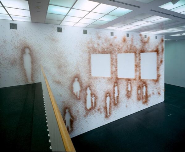 A mural that covers a large wall depicts the outline of 11 people and 3 squares in an orange-brown with sprays of that color around the wall.