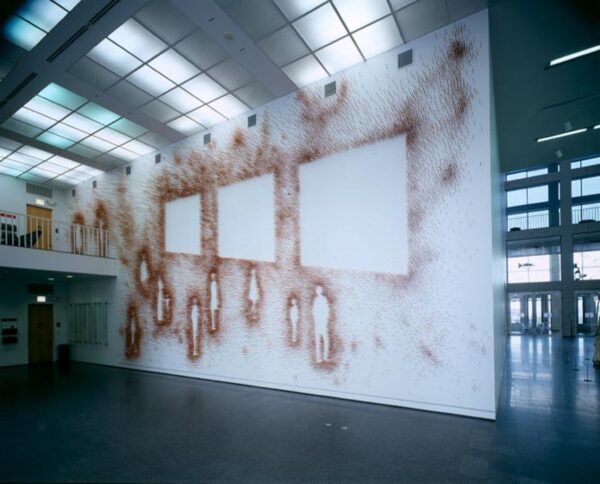 A mural that covers a large wall depicts the outline of 11 people and 3 squares in an orange-brown with sprays of that color around the wall.