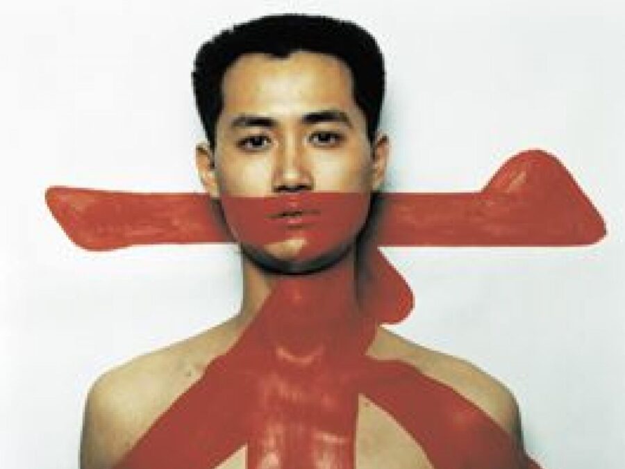 A photo of a shirtless man staring straight at the viewer with a red character over his body