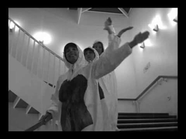 Three people in white coveralls descend the MCA staircase with their left arms in the air