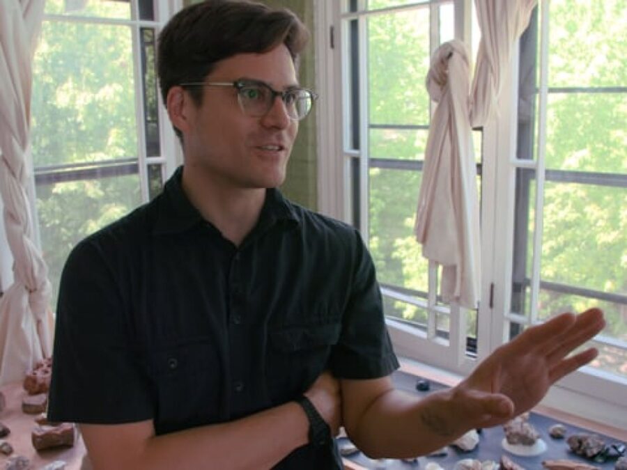 A male-presenting person in the corner of a room with windows on both sides