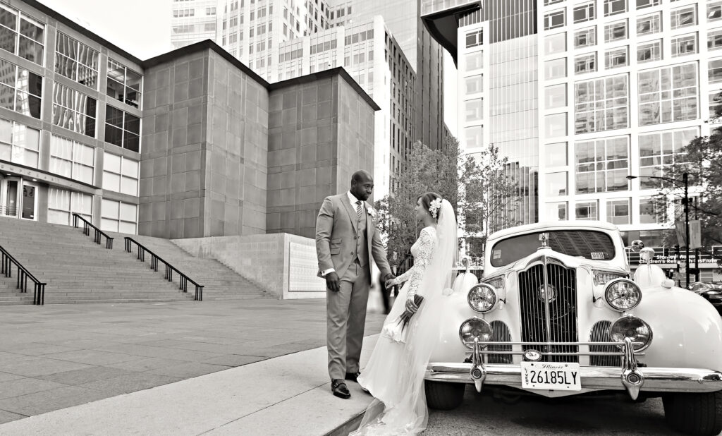 A wedding bride and groom poses next to a vintage white car in front of the MCA