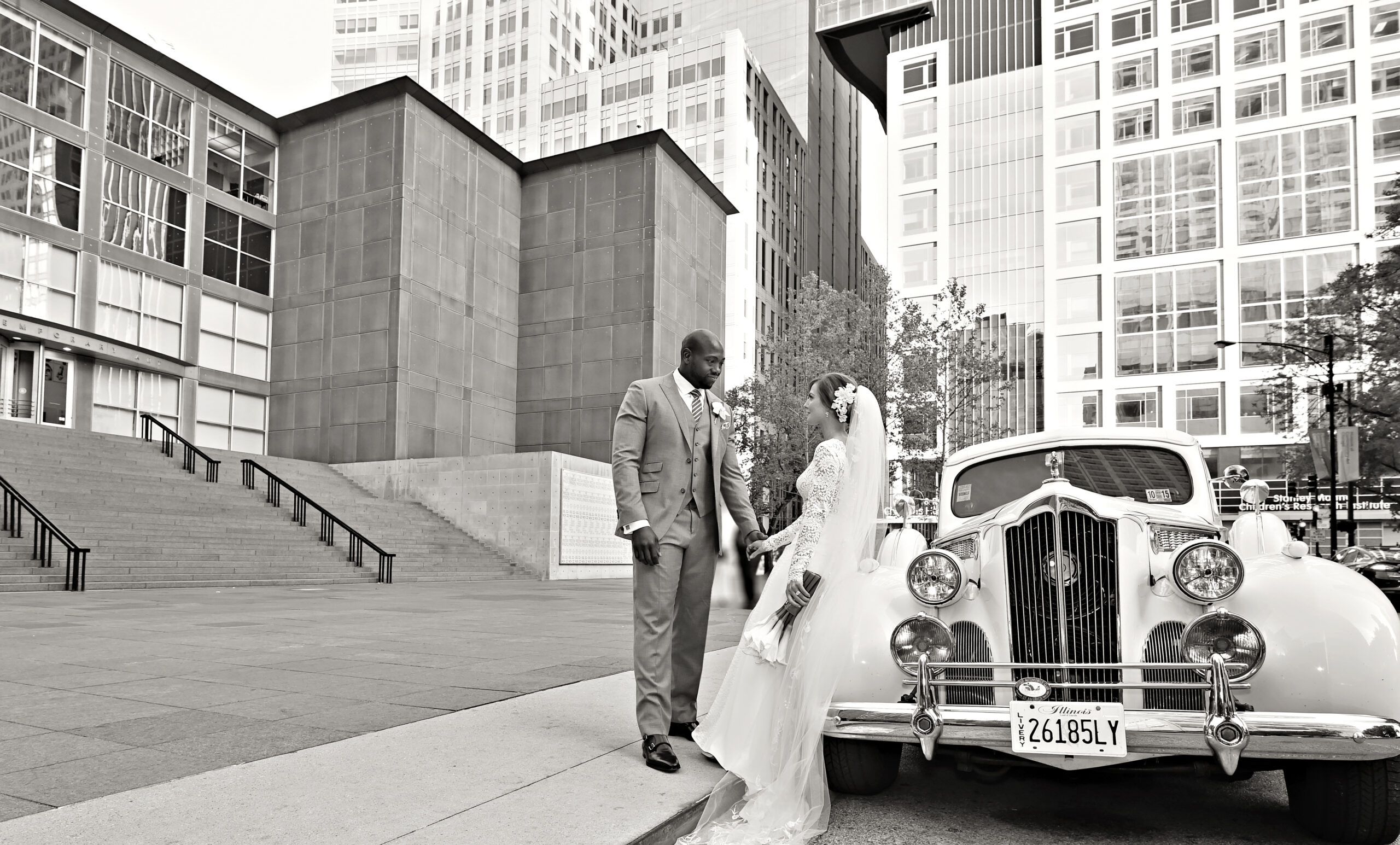 A wedding bride and groom poses next to a vintage white car in front of the MCA