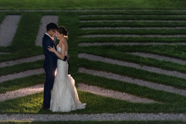 A bride and groom hold each other outdoors in a garden over a stone formation of lines