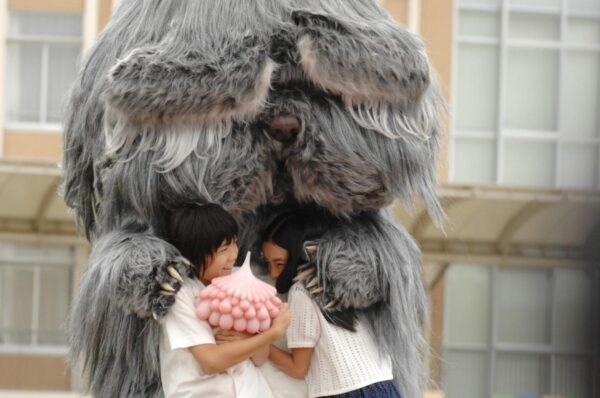 A giant furry grey animal hugs two kids