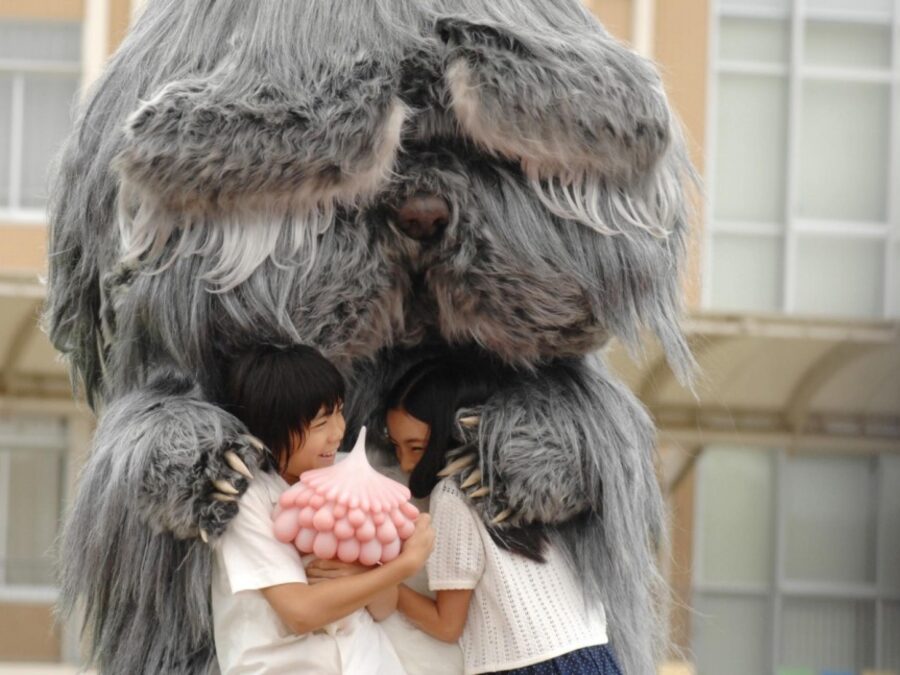 A giant furry grey animal hugs two kids