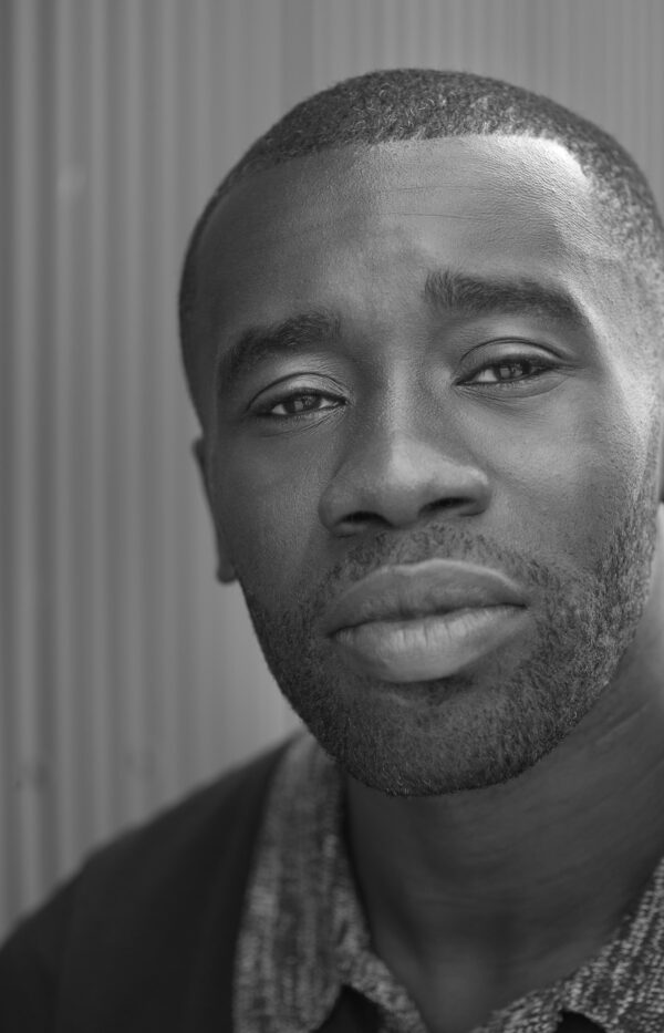 A young Black man with a closely shaved head and bear looks directly at the viewer