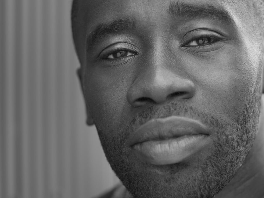 A young Black man with a closely shaved head and bear looks directly at the viewer