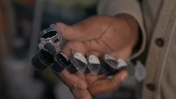A right hand holds a paint pot strip with black paint in each