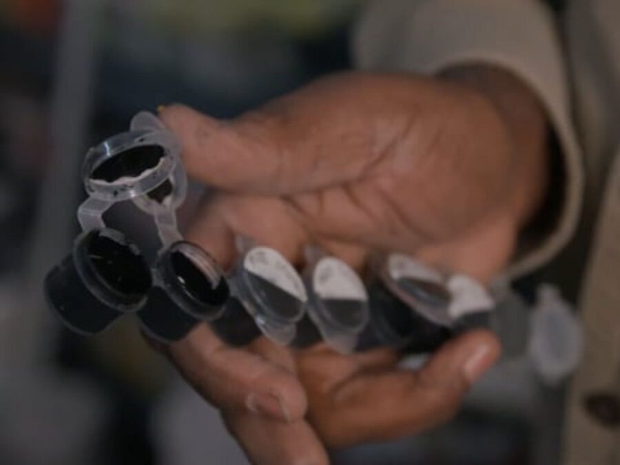 A right hand holds a paint pot strip with black paint in each
