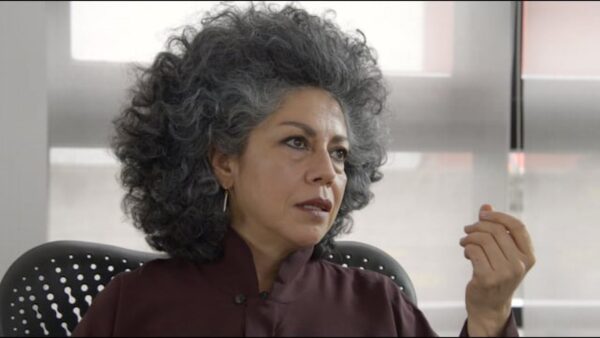 A still of Doris Salcedo, a female presenting person with light brown skin and a salt and pepper afro, speaking.