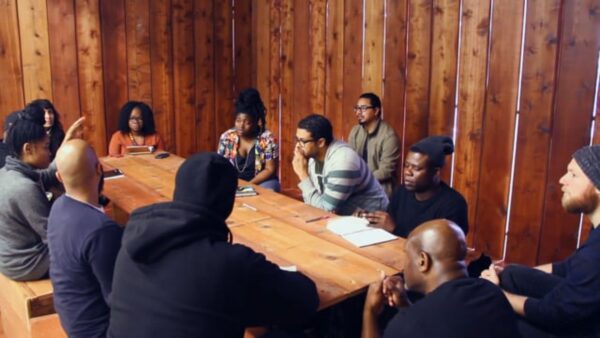 A group of people sit around a wooden table in a wood-paneled room