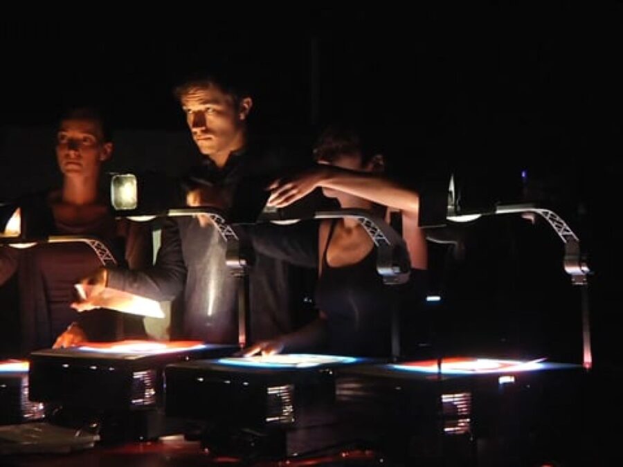 Three people work with projectors in a dark room