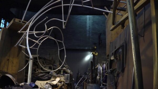A twisted silver metal sculpture in a dark warehouse studio
