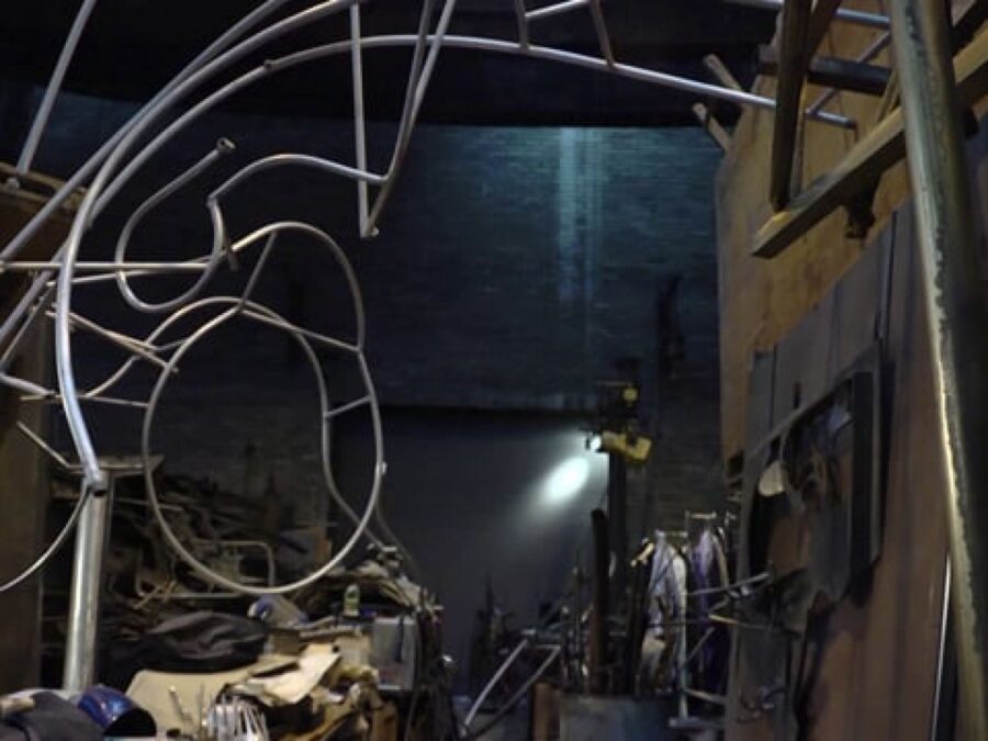 A twisted silver metal sculpture in a dark warehouse studio