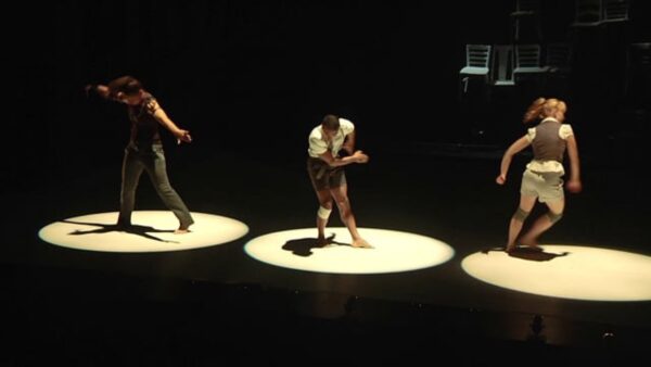 Three dancers in various positions lit only by three spotlights on a dark stage