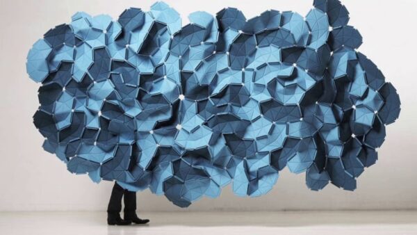 A persons legs can just be seen from behind a blue fabric cloud-like form hanging in a white room