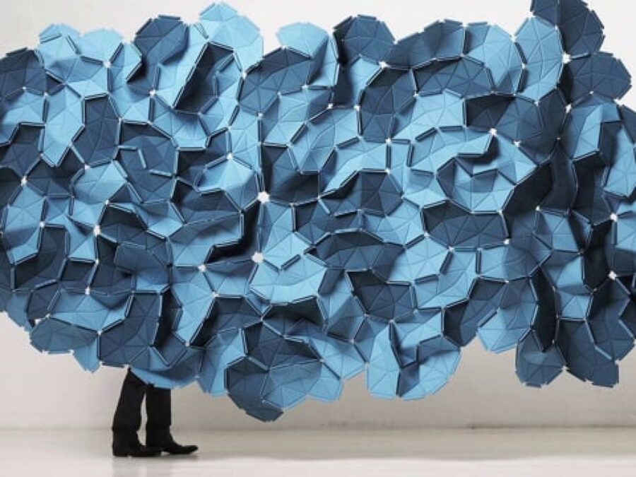 A persons legs can just be seen from behind a blue fabric cloud-like form hanging in a white room