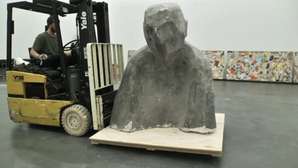A grey, abstracted bust on a forklift in a gallery space