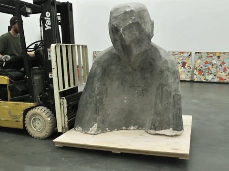 A grey, abstracted bust on a forklift in a gallery space