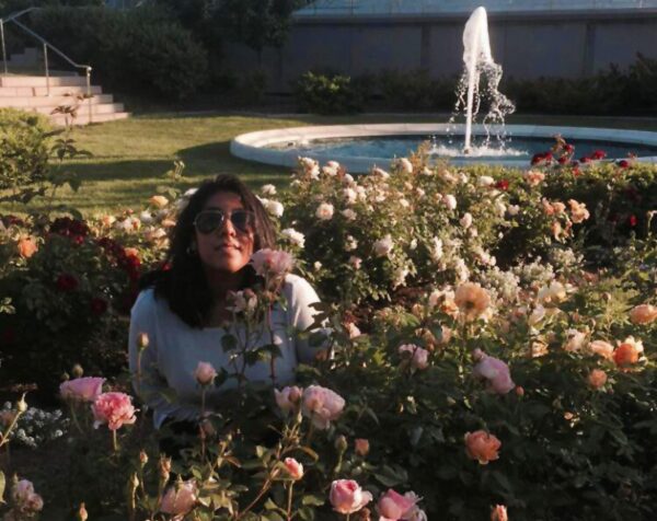 A person poses in the middle of a flower field near a large fountain